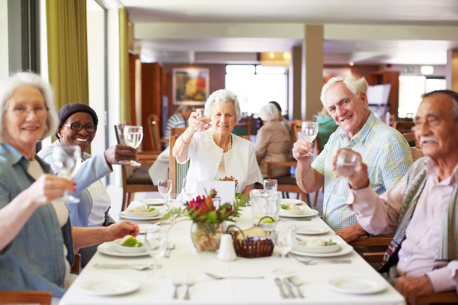 A group of seniors raise their glasses for a toast while enjoying a restaurant-style dining experience together in a retirement home